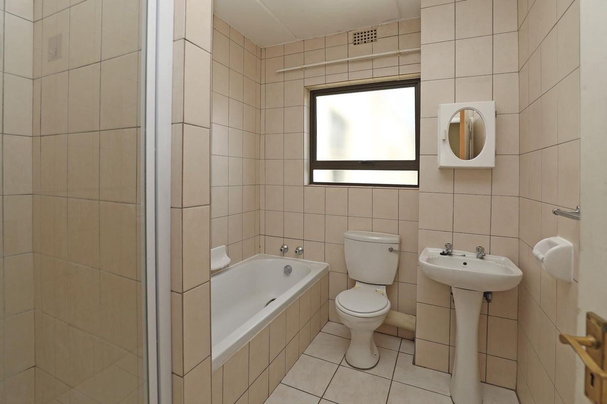 A functional bathroom featuring a pedestal basin, a standard bathtub, and a toilet, finished with neutral wall tiles and a window for natural light.