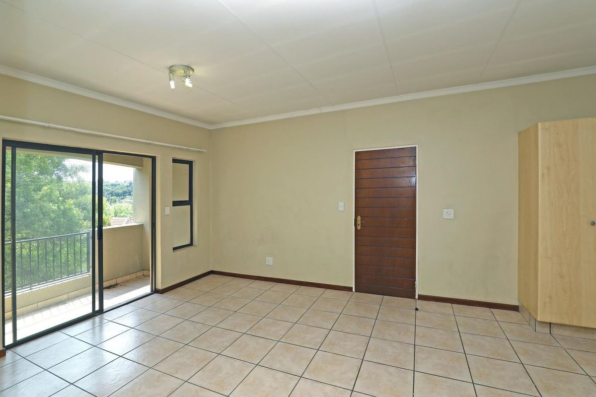 A spacious, empty bedroom featuring tiled flooring, a built-in wardrobe, and sliding glass doors leading to a private balcony.
