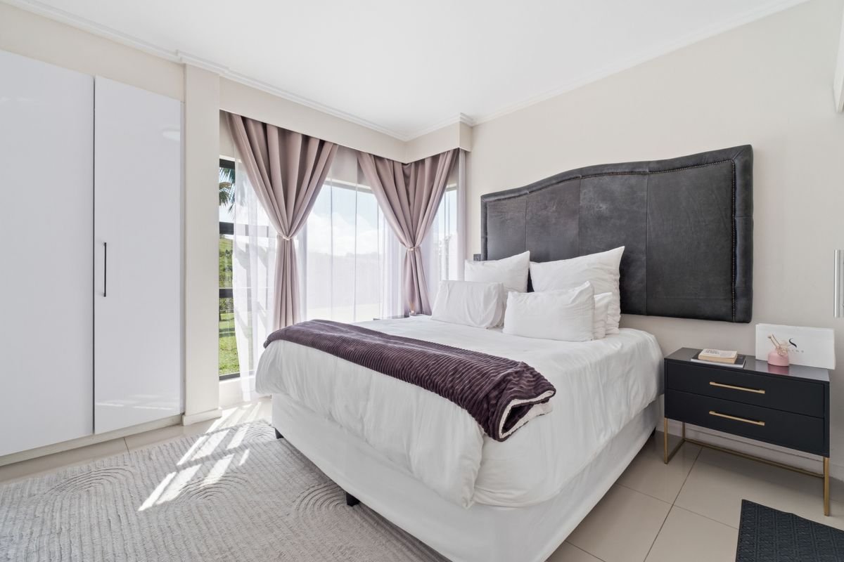 A well-maintained bedroom featuring tiled flooring, a large built-in wardrobe, and a corner window that allows for natural light.