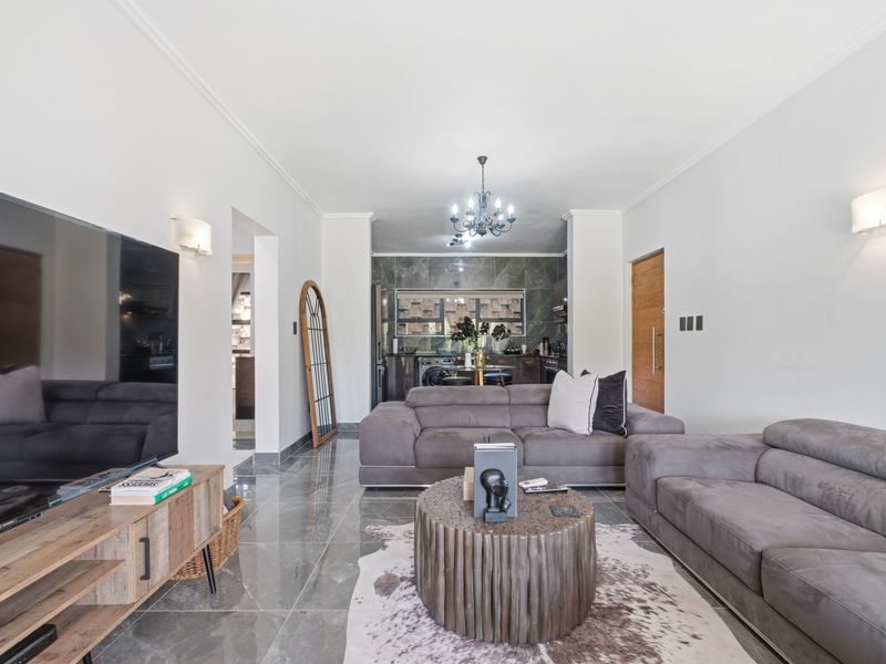 Modern open-plan living area featuring polished tiled floors, contemporary kitchen cabinetry with stone backsplash, and elegant lighting fixtures throughout the space.