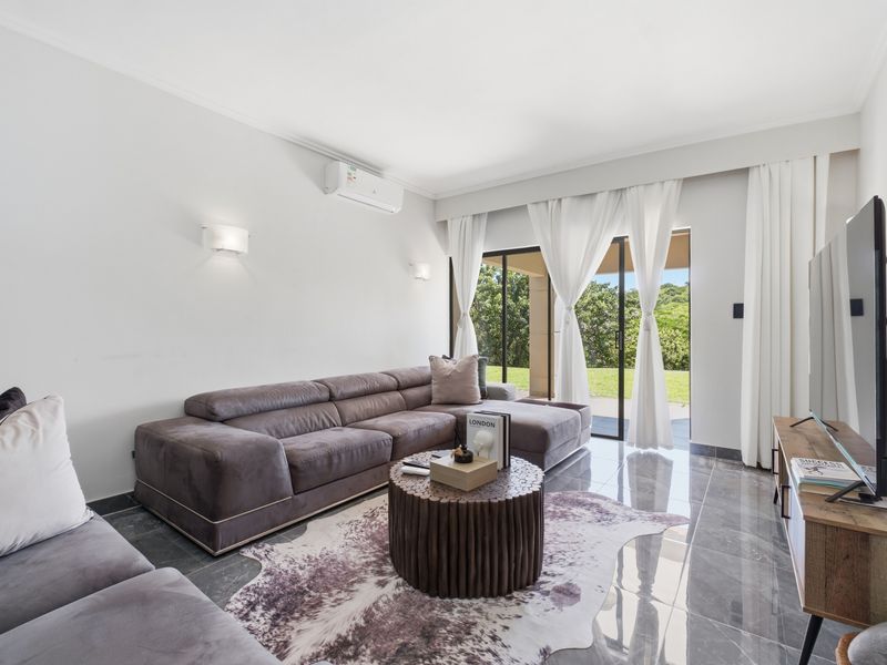 A bright and modern living room featuring polished tiled floors, split-system air conditioning, and large sliding glass doors that open to an outdoor area.