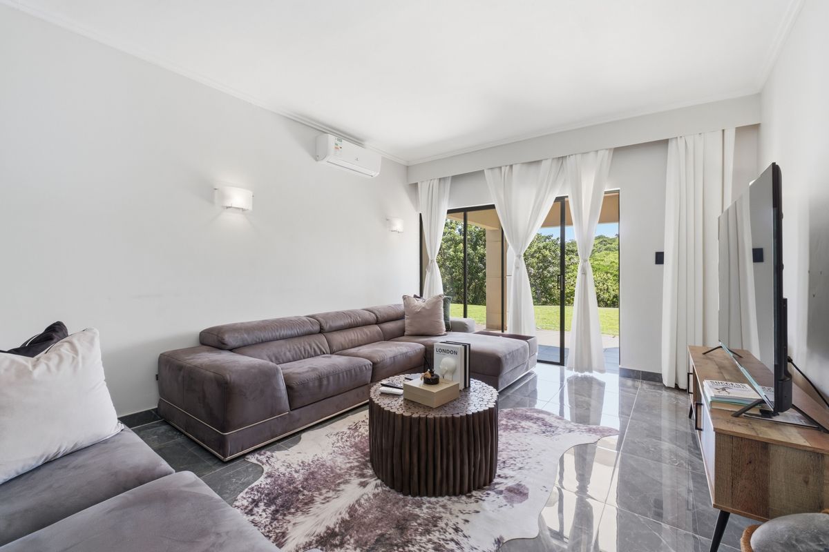 A bright and modern living room featuring polished tiled floors, split-system air conditioning, and large sliding glass doors that open to an outdoor area.