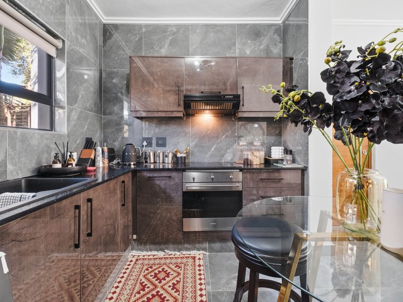 Modern kitchen featuring dark wood-finish cabinetry, stone countertops, integrated oven, extractor fan, and sleek grey marble-effect wall tiling.