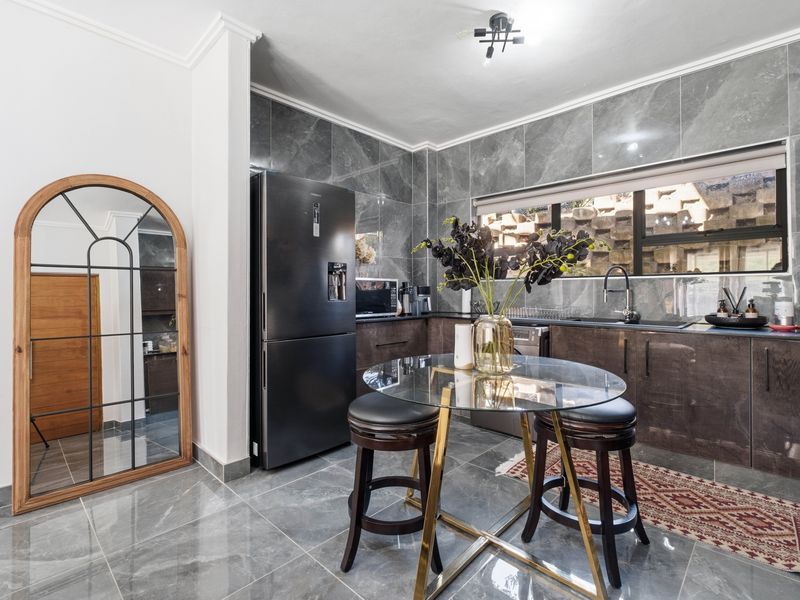 Modern kitchen featuring high-gloss cabinetry, marble-look wall and floor tiles, and a sleek undermount sink with a contemporary mixer tap.