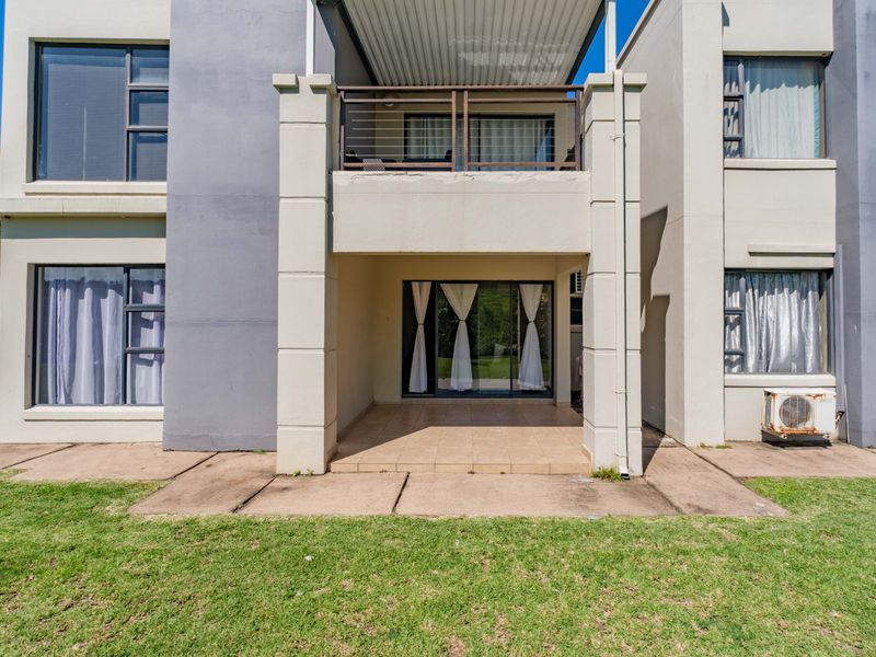 Rear view of the apartment building featuring a ground-floor tiled patio, an upper-level balcony, and sliding glass doors leading into the living space.