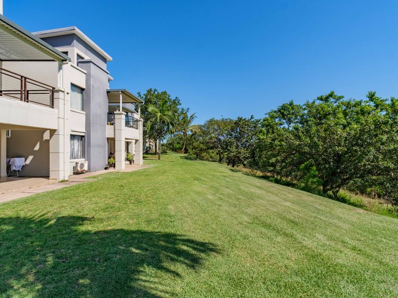Rear view of the apartment building featuring a spacious lawn, private balconies, and established trees in a well-maintained residential setting.