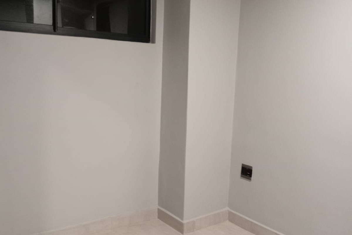 A clean, empty bedroom featuring neutral tiled flooring, freshly painted walls, and a modern black-framed window.