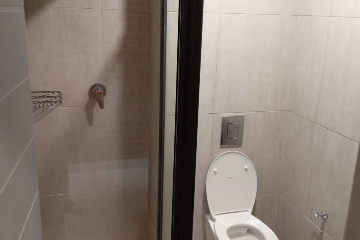 Modern bathroom featuring a glass-enclosed shower with rainfall showerhead, wall-mounted toilet with concealed cistern, and neutral floor-to-ceiling tiling.