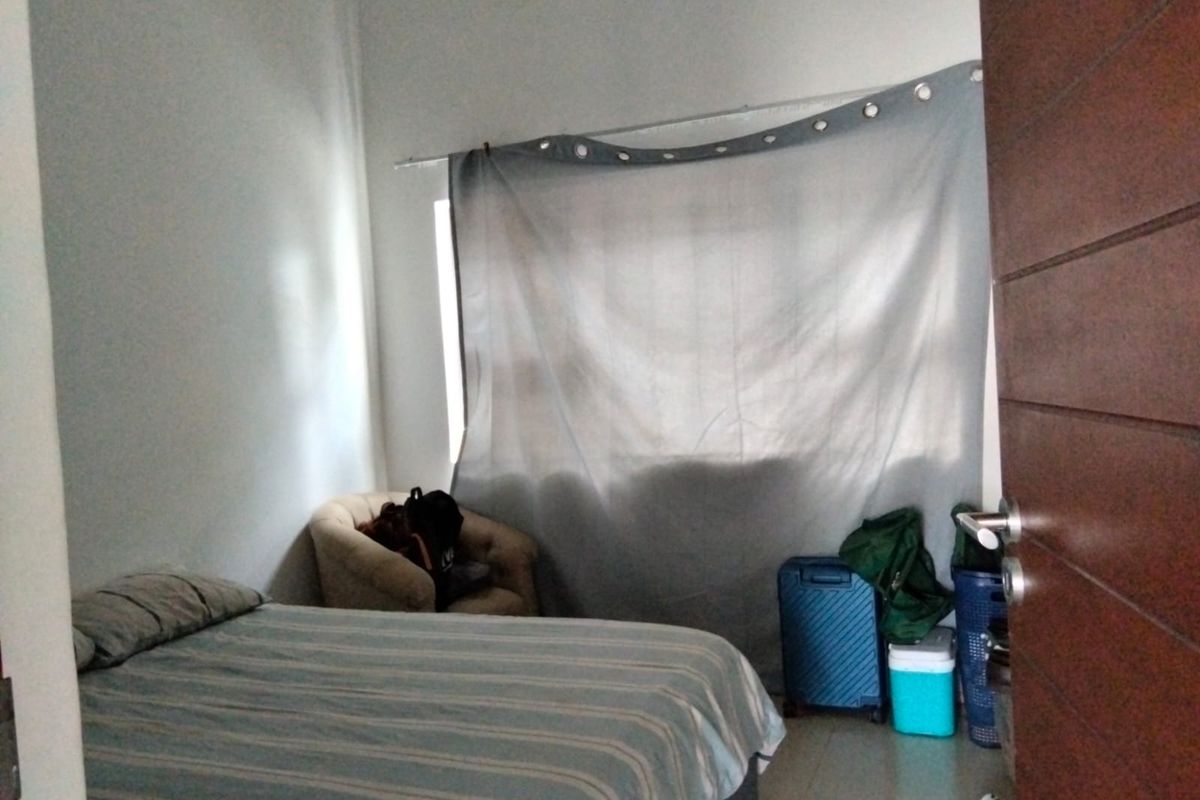 A standard bedroom featuring a window with curtain and a wooden door, providing a functional living space.