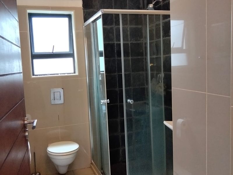 A modern bathroom featuring a glass shower enclosure, wall-mounted toilet, and contrasting dark and light tiled finishes.