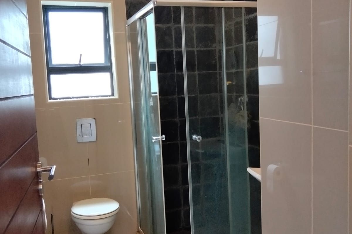 A modern bathroom featuring a glass shower enclosure, wall-mounted toilet, and contrasting dark and light tiled finishes.
