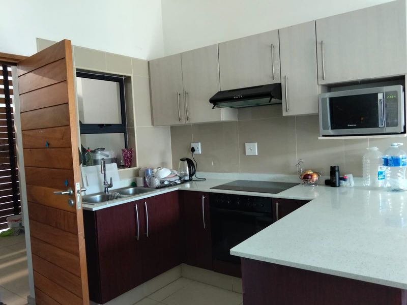 Modern kitchen featuring two-tone cabinetry, stone countertops, integrated appliances including an oven, hob, and extractor fan, with a tiled backsplash.