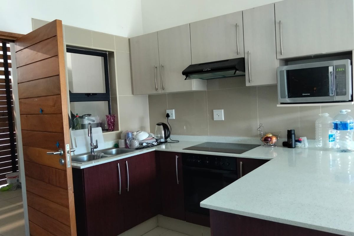 Modern kitchen featuring two-tone cabinetry, stone countertops, integrated appliances including an oven, hob, and extractor fan, with a tiled backsplash.