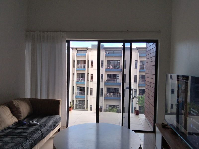 A living room featuring a large sliding glass door that opens onto a tiled balcony with views of the surrounding apartment complex.