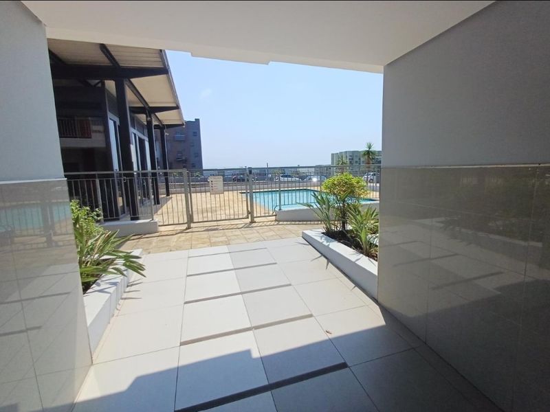A view of the communal swimming pool area featuring tiled patio flooring, metal safety fencing, and built-in planter boxes.