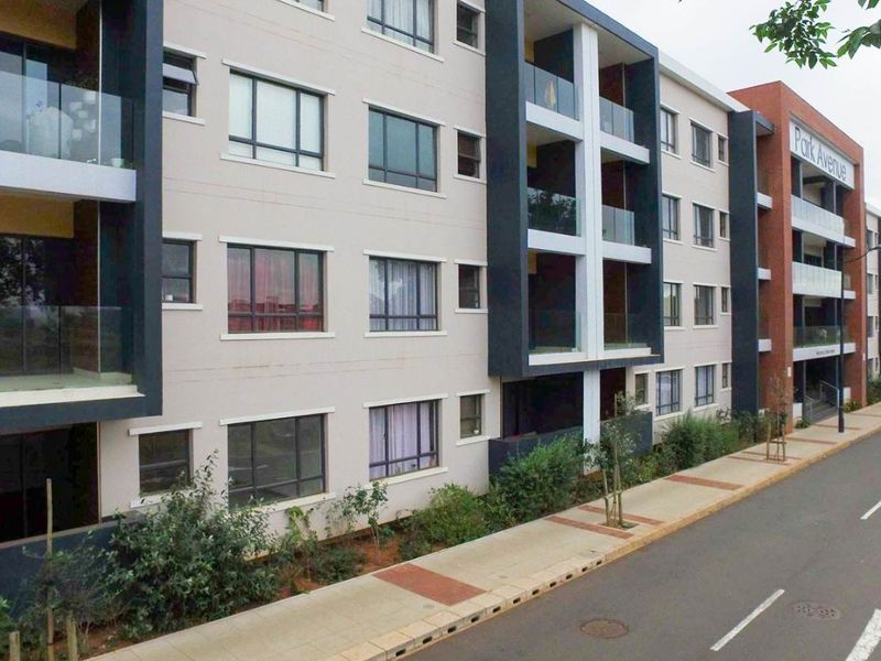 A modern multi-story apartment complex featuring contemporary facade design, glass-fronted balconies, and a well-maintained street-level sidewalk and landscaping.