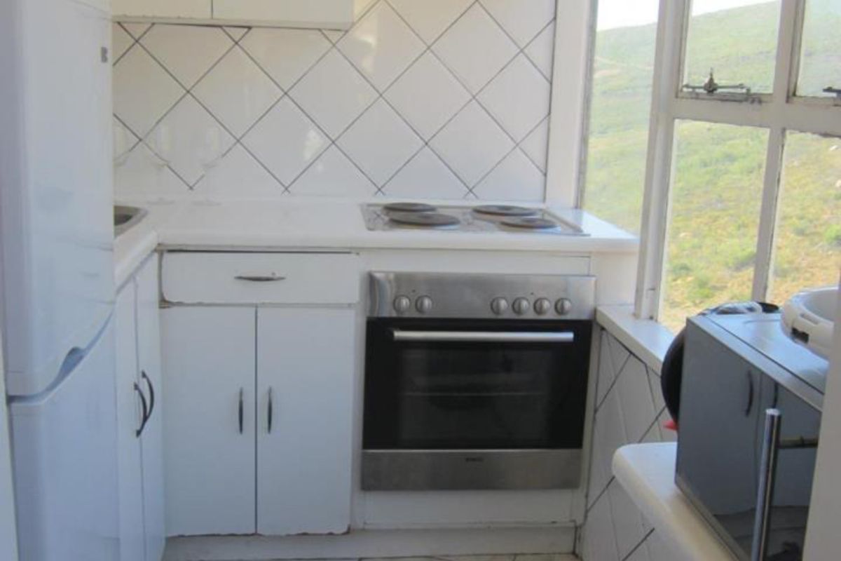 Compact kitchen featuring white cabinetry, built-in oven and hob, tiled splashback, and large windows offering scenic mountain views.