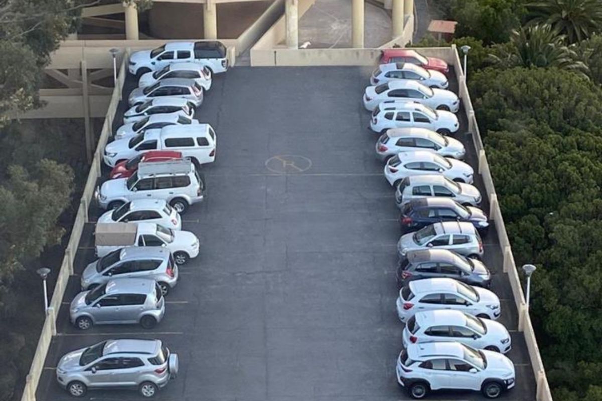 An elevated aerial view of an outdoor parking area serving an apartment building, featuring marked parking bays and surrounding greenery.