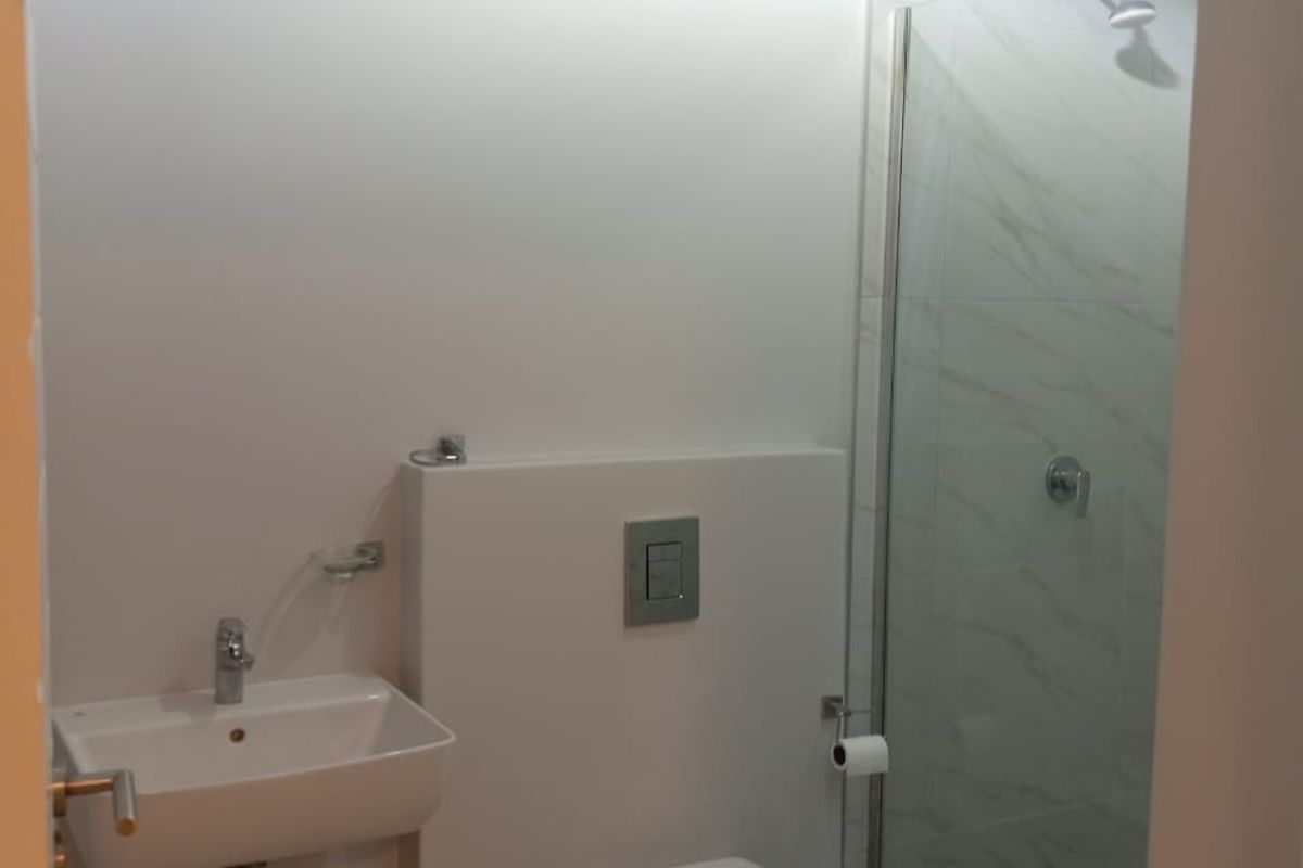 Modern bathroom featuring a wall-mounted basin, concealed cistern toilet, and a glass-enclosed shower with marble-look wall tiles.