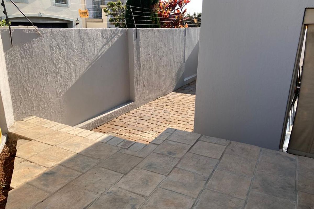 A paved side walkway and patio area featuring high perimeter boundary walls with integrated electric fencing for added security.
