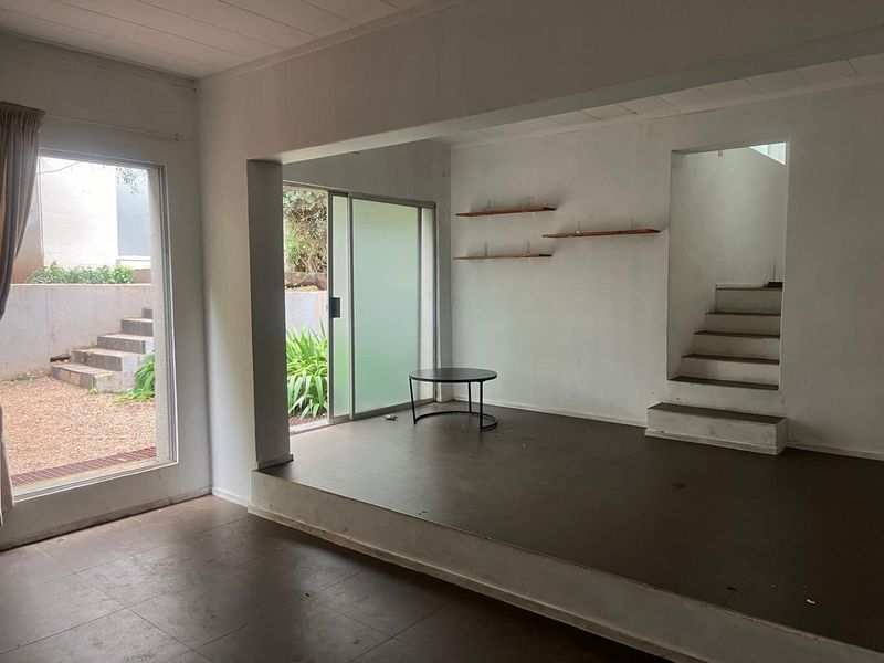 Spacious living area featuring a raised platform, built-in staircase, and sliding glass doors providing direct access to the outdoor garden area.