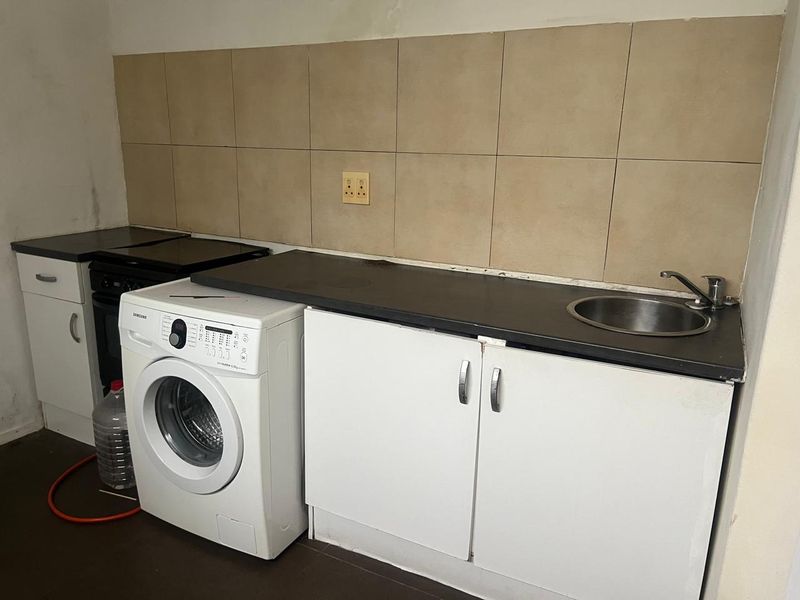 A functional laundry area featuring built-in cabinetry, a stainless steel sink, tiled splashback, and space for a washing machine and stove.