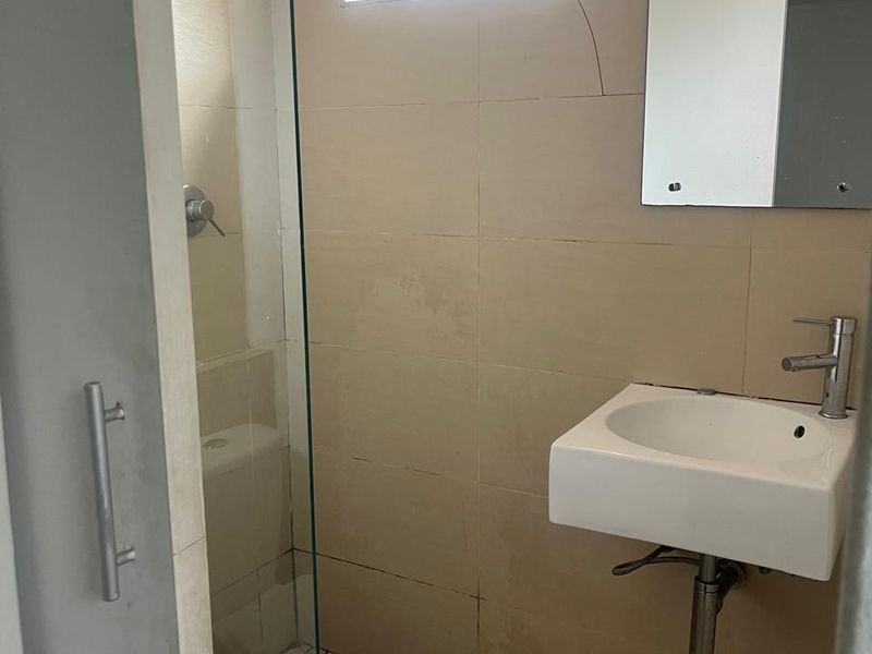 Compact bathroom featuring a wall-mounted basin, glass shower enclosure, and tiled finishes. The space requires maintenance to address cracked and stained tiling.