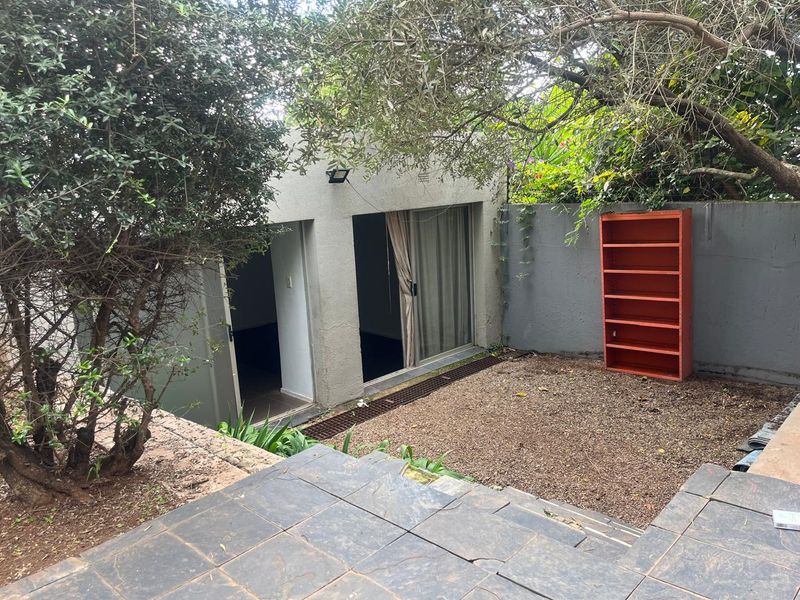 Rear exterior view of the cottage featuring a gravel courtyard, stone tiled patio area, and sliding door access to the interior.