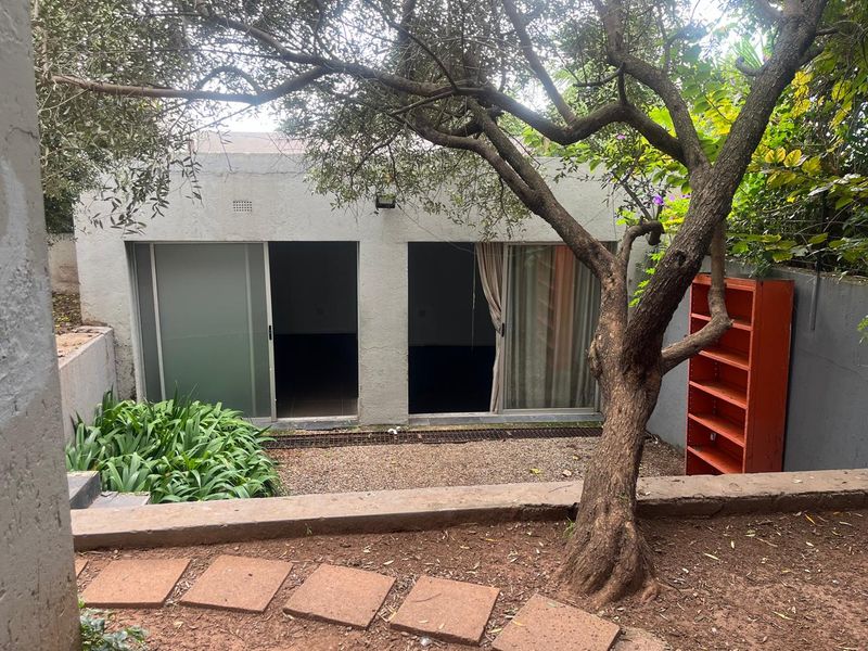 Rear exterior view of the cottage featuring sliding glass doors, a gravel courtyard area, and established garden landscaping.