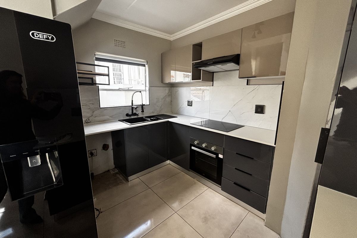 Modern kitchen featuring sleek dark grey cabinetry, marble-look splashback, built-in oven, hob, extractor fan, and a double sink with a contemporary faucet.