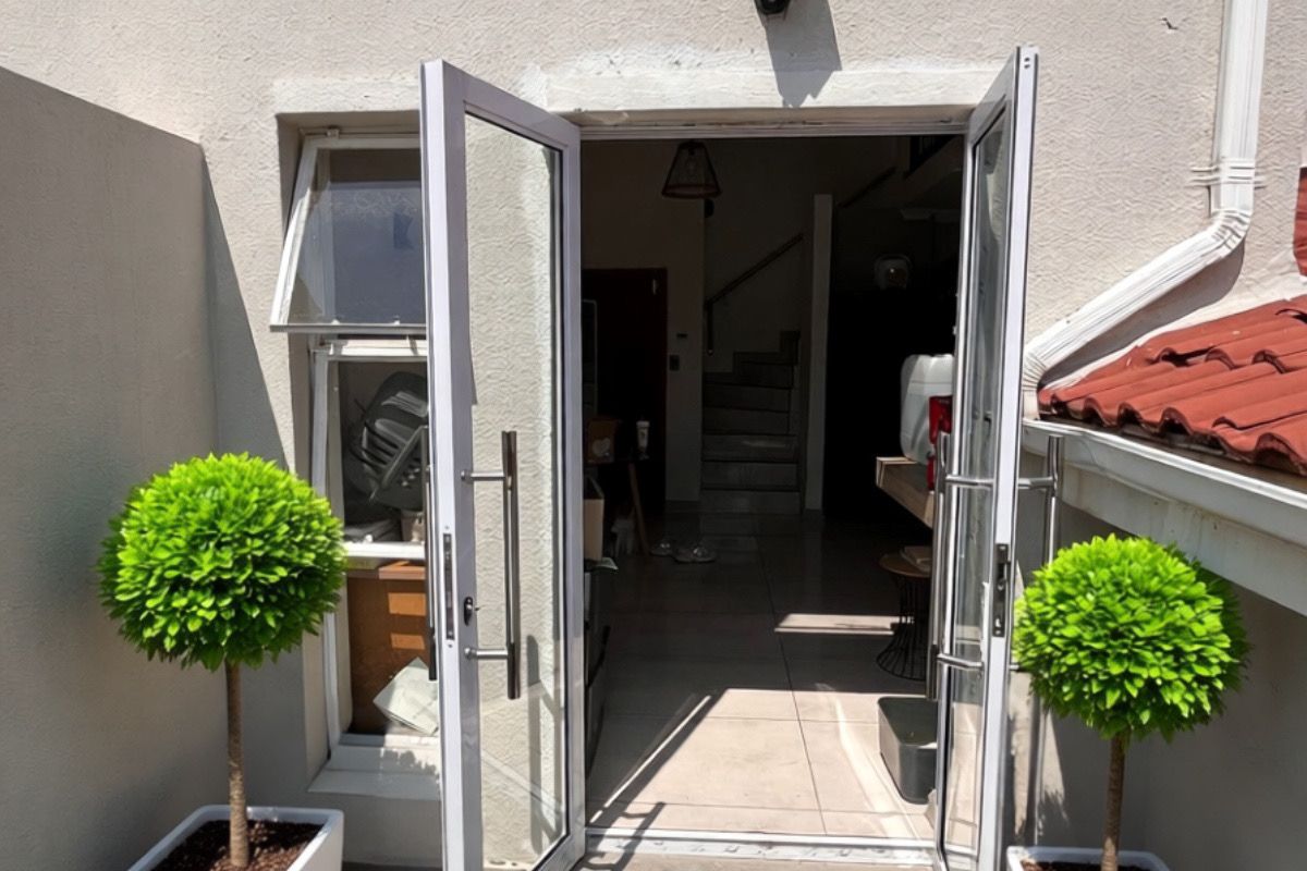 Exterior view of a ground-level entrance featuring double glass doors, tiled patio area, and wall-mounted lighting fixture.