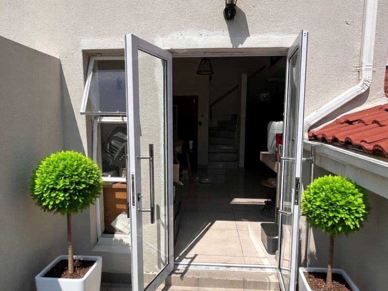 Exterior view of a ground-level entrance featuring double glass doors, tiled patio area, and wall-mounted lighting fixture.
