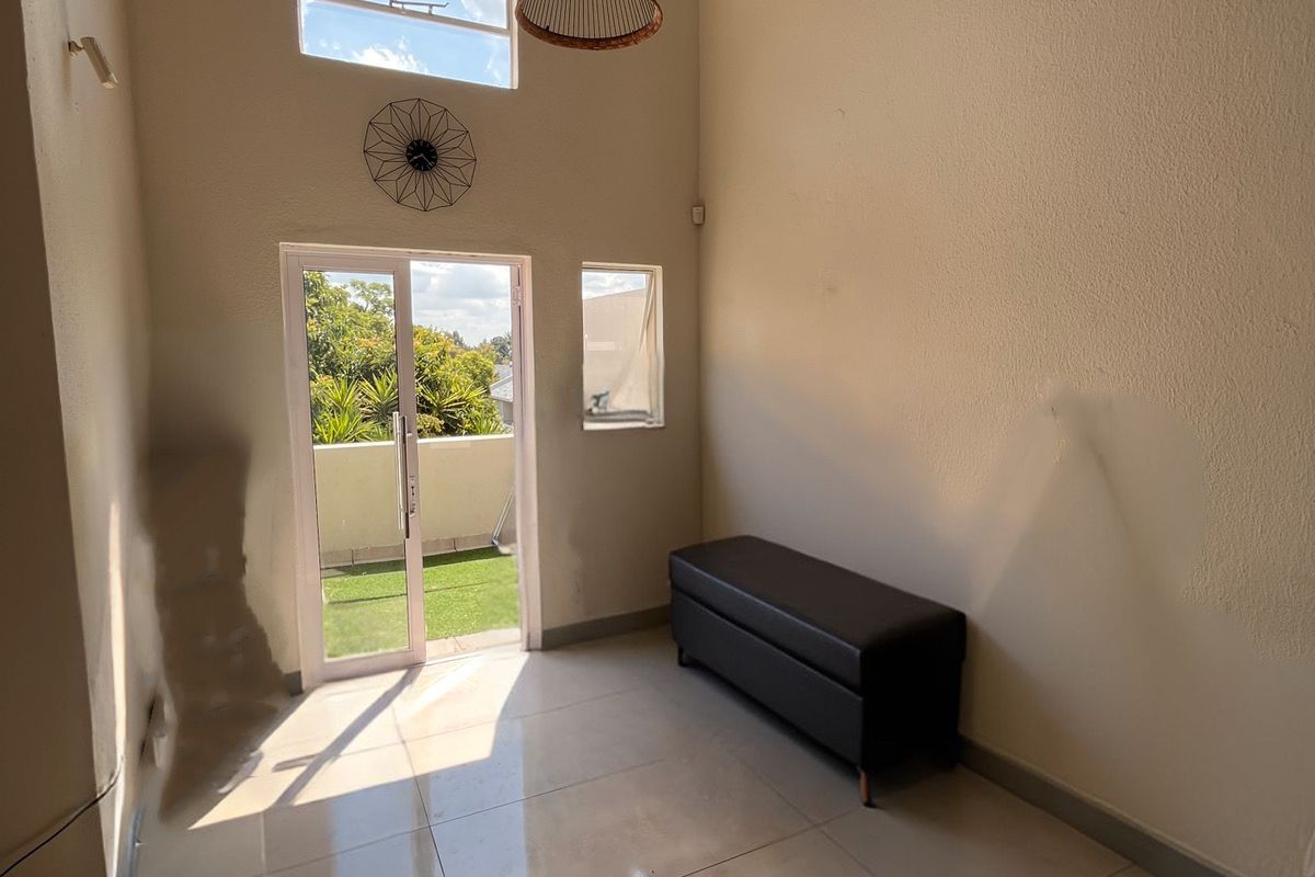 A bright living area featuring high vaulted ceilings, large windows, tiled flooring, and direct access to a private balcony.