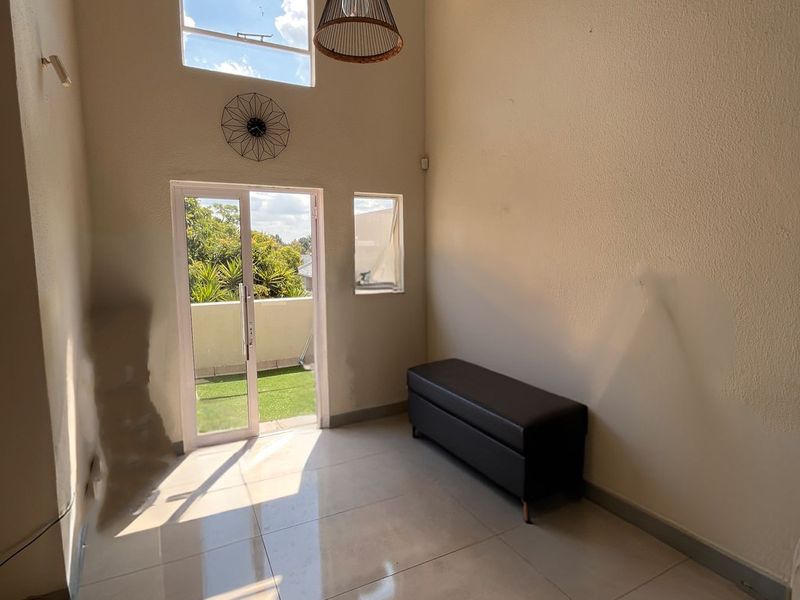 A bright living area featuring high vaulted ceilings, large windows, tiled flooring, and direct access to a private balcony.