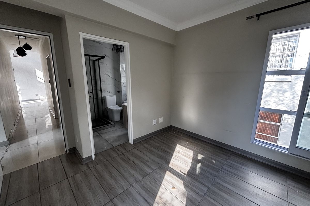 A bright bedroom featuring wood-look tile flooring, large windows, and an en-suite bathroom with modern finishes.