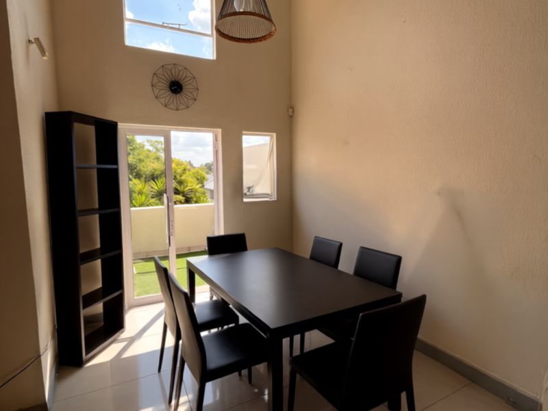 A bright dining area featuring high vaulted ceilings, tiled flooring, and direct access to a private balcony through a glass door.