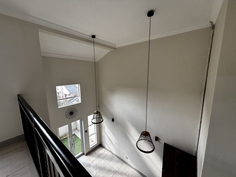 A high-ceilinged entrance foyer featuring tiled flooring, modern pendant lighting, and a glass door leading to an outdoor area.