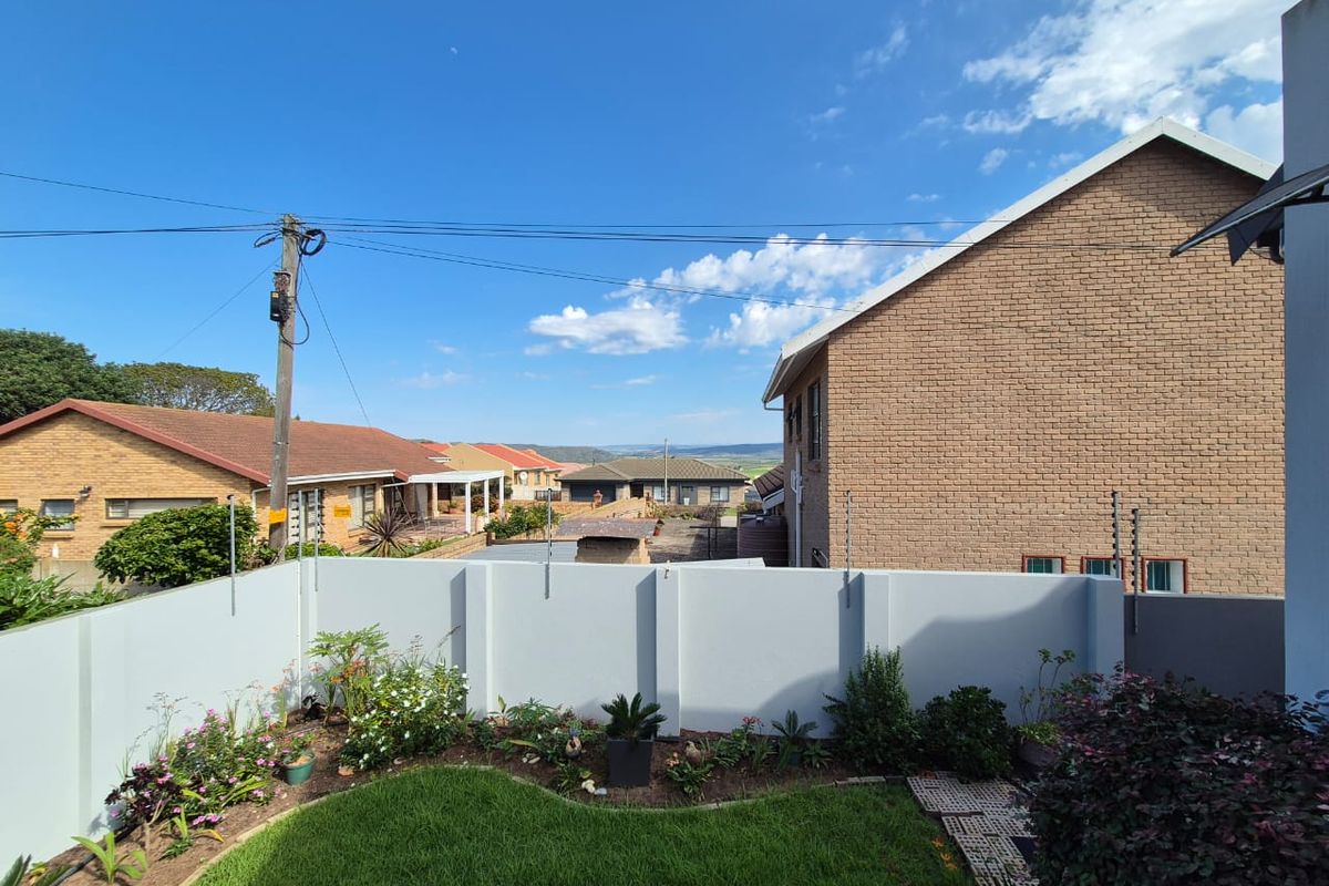 A view of the rear garden featuring a manicured lawn, landscaped garden beds, and a perimeter wall with integrated electric fencing.