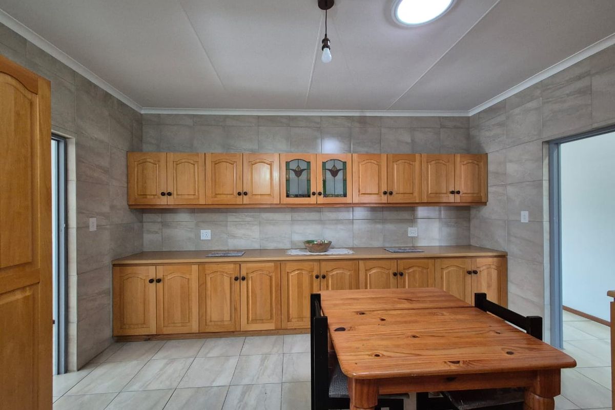 A functional kitchen featuring extensive wooden cabinetry, tiled walls, and neutral floor tiles, providing ample storage and workspace.