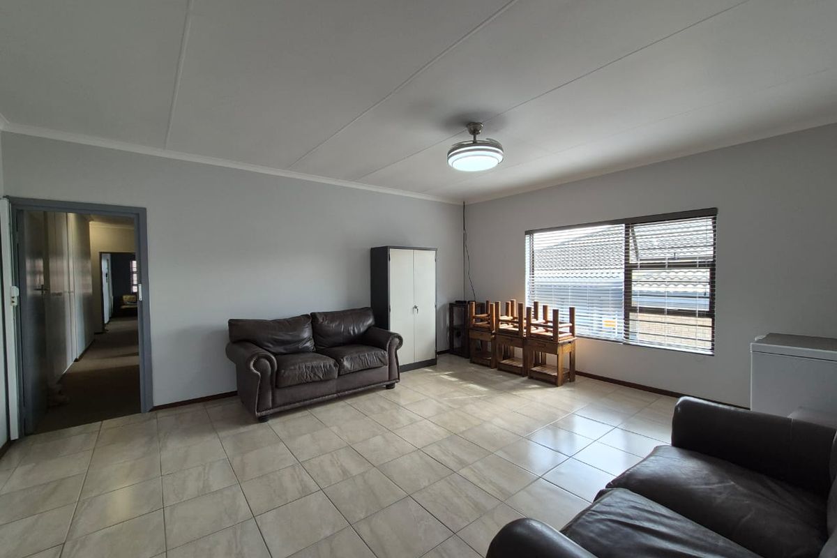 A spacious living room featuring neutral tiled flooring, a ceiling fan, and large windows with horizontal blinds, providing a bright and functional living space.