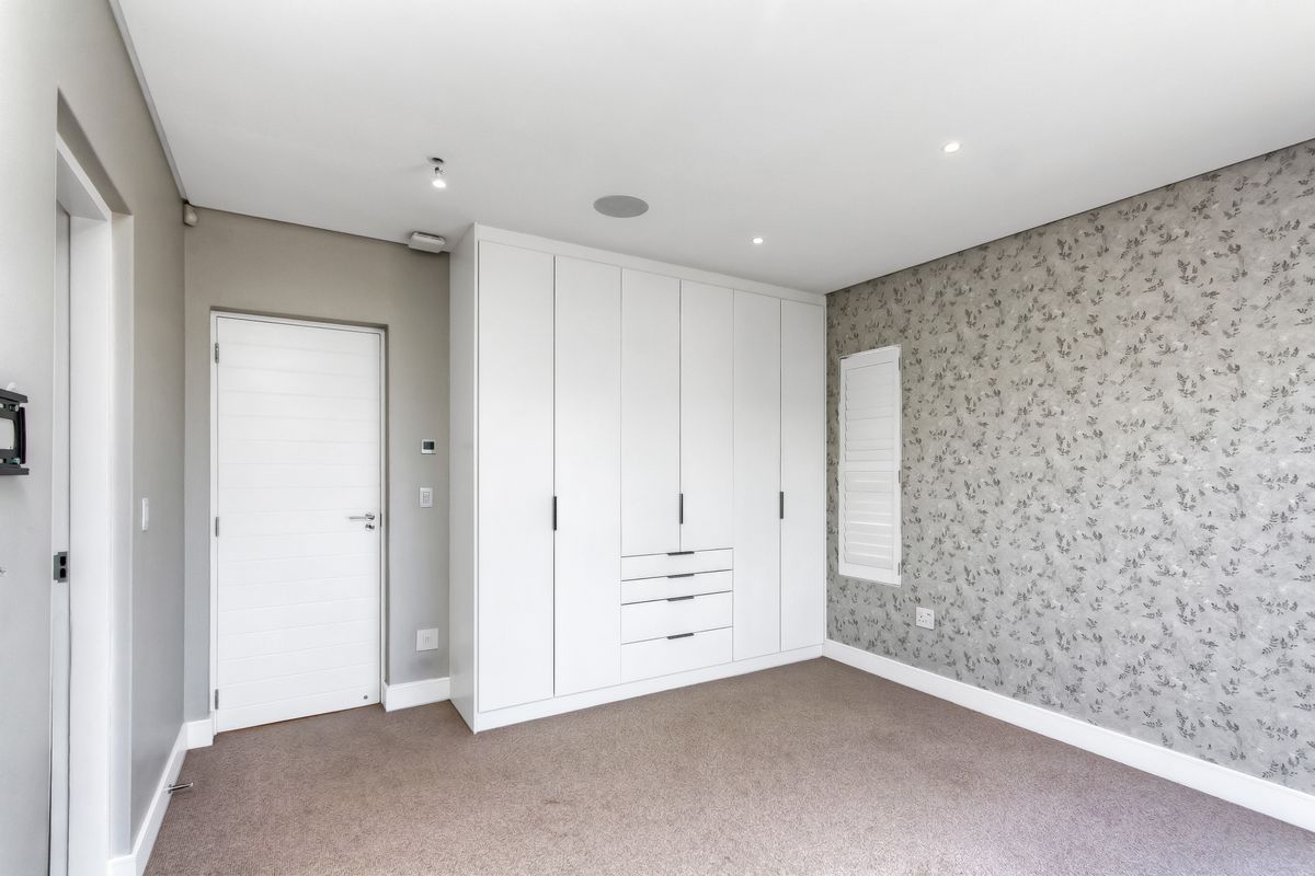 A well-maintained bedroom featuring built-in floor-to-ceiling cabinetry, recessed downlighting, and a decorative feature wall with neutral carpeting.