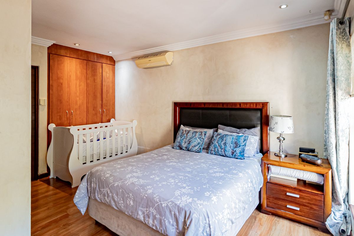 A bedroom featuring built-in wooden cabinetry, laminate flooring, and a wall-mounted air conditioning unit.