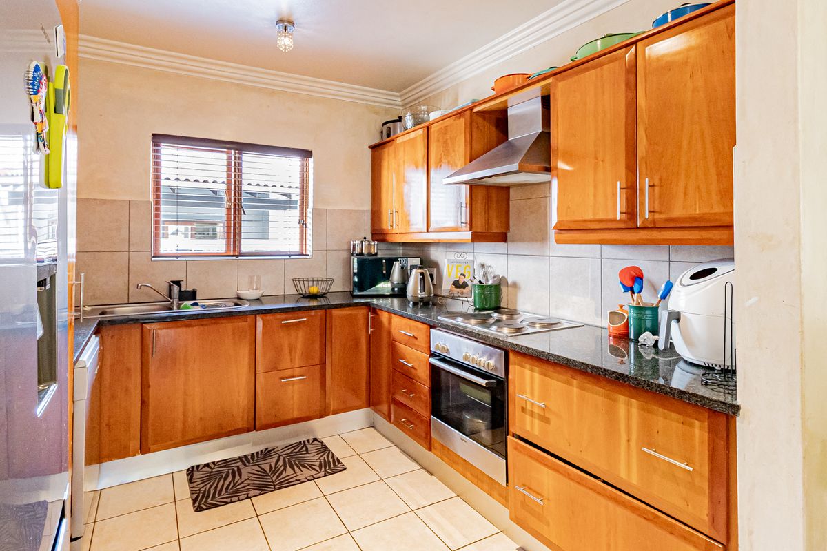 A functional kitchen featuring wooden cabinetry, granite countertops, a built-in oven, hob, and extractor fan, complemented by tiled flooring and a window for natural light.