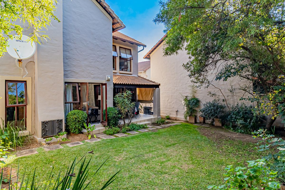 Rear view of the townhouse featuring a private garden, paved walkway, and a covered patio area accessible through double doors.