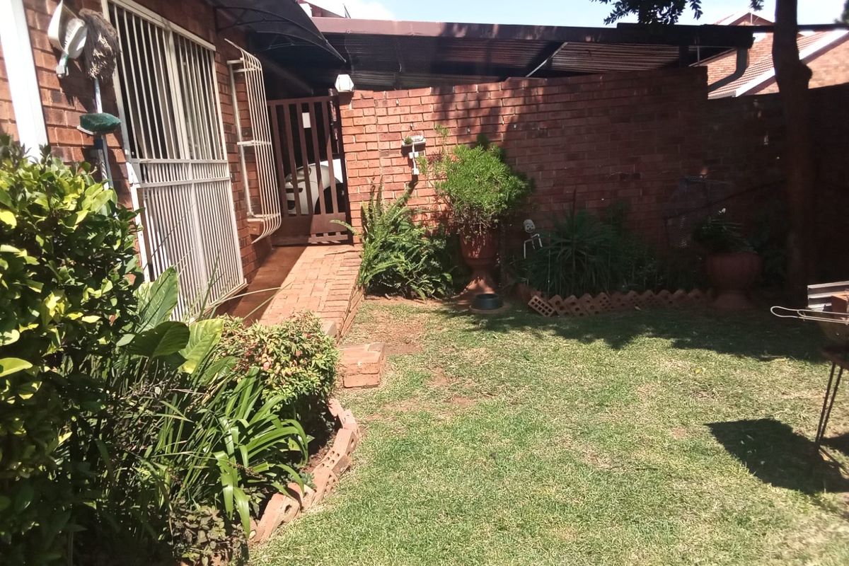 A private rear garden area featuring a brick boundary wall, paved walkway, and a covered patio section attached to the townhouse structure.