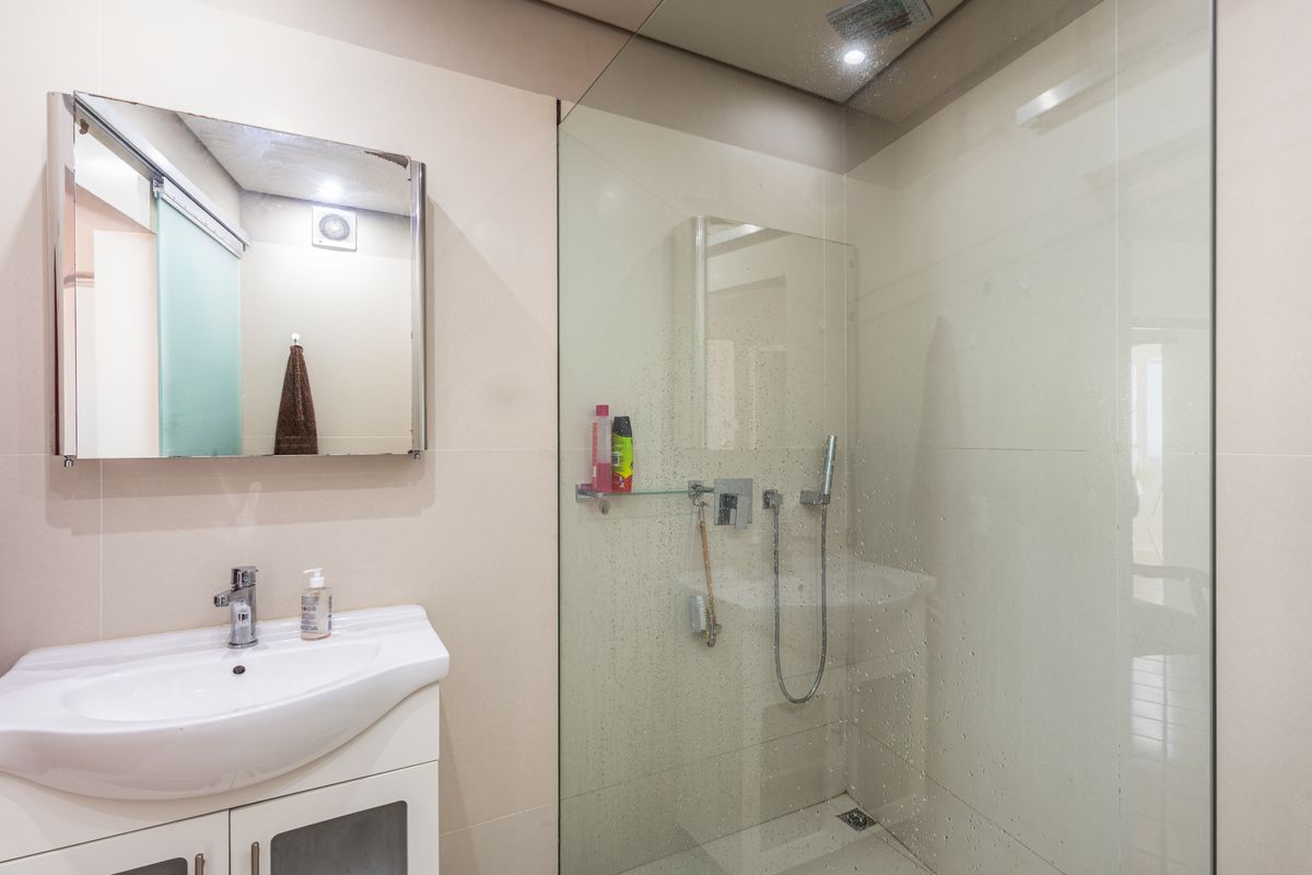Modern bathroom featuring a glass-enclosed walk-in shower, wall-mounted vanity with integrated basin, and a framed mirror.