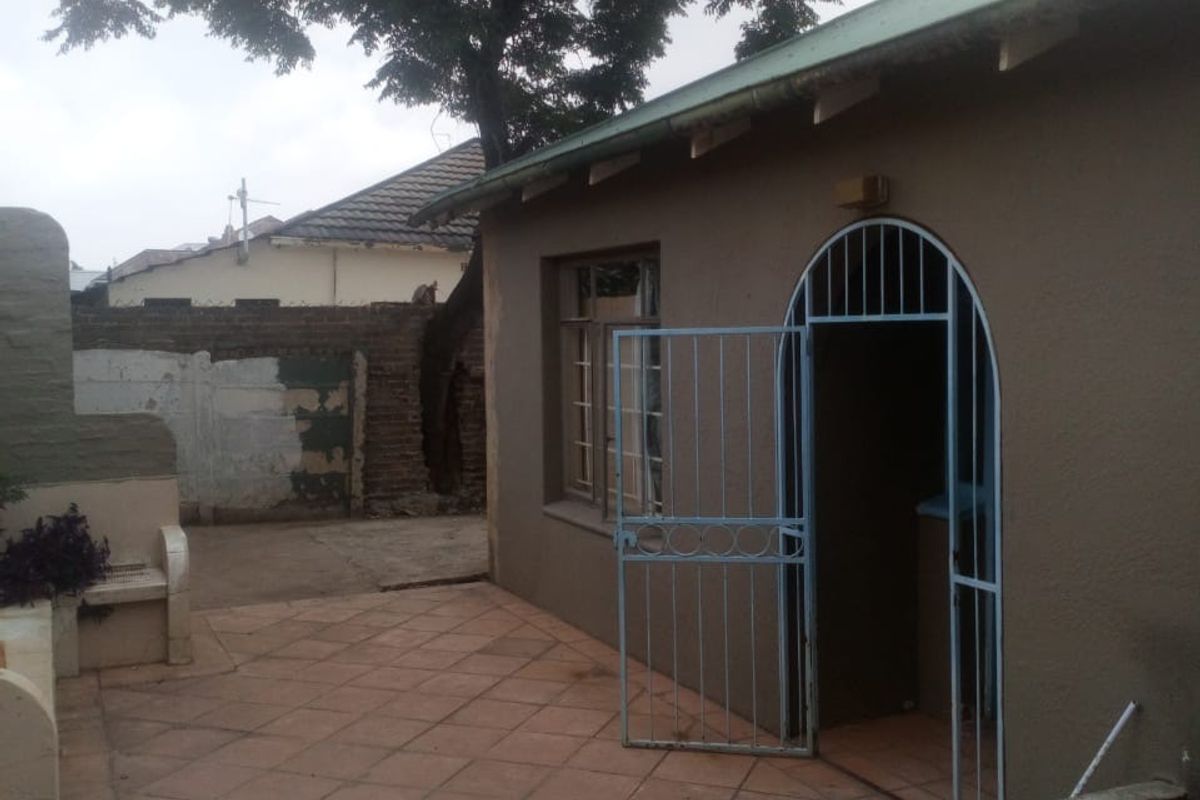 A rear exterior view of the property featuring a tiled patio area, arched security gate, and a weathered boundary wall.