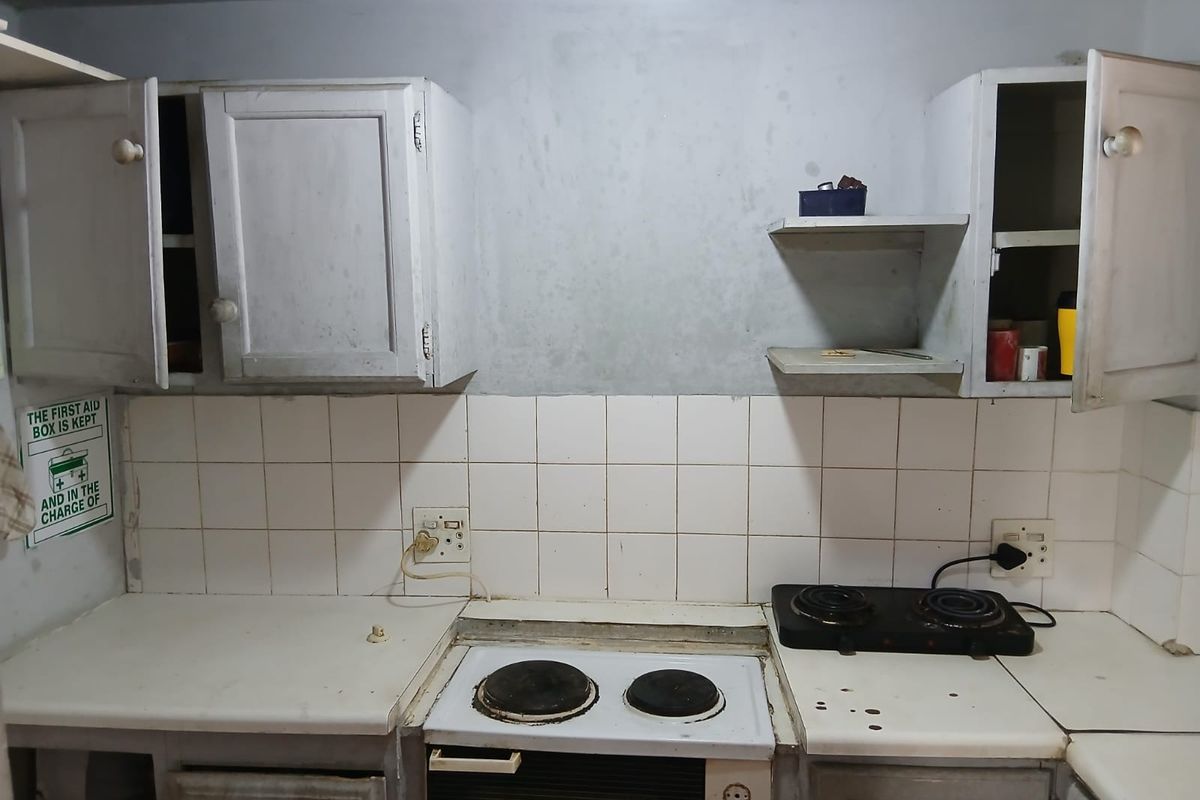A dated kitchen area featuring basic cabinetry, tiled splashbacks, and a built-in electric stove, requiring cosmetic updates and refurbishment.