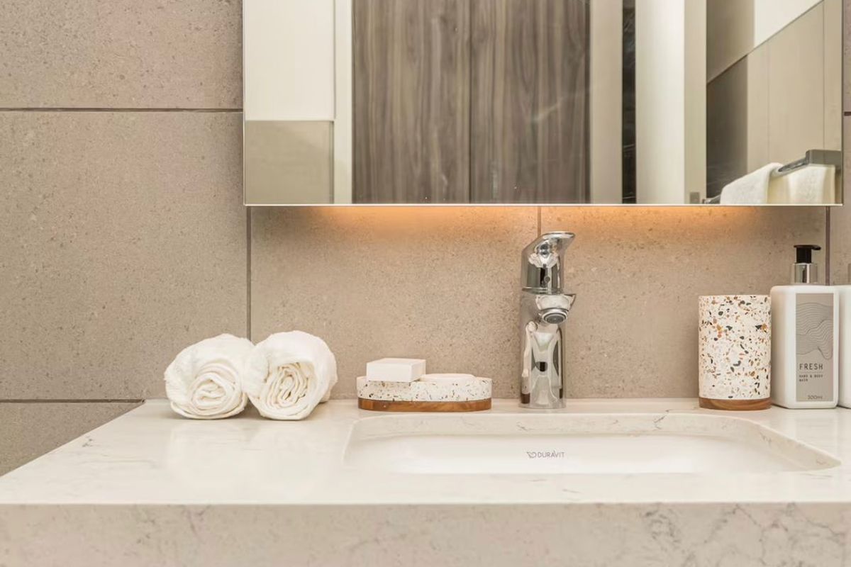 Modern bathroom vanity featuring a stone countertop, integrated basin, chrome faucet, and wood-grain cabinetry with a large wall-mounted mirror.