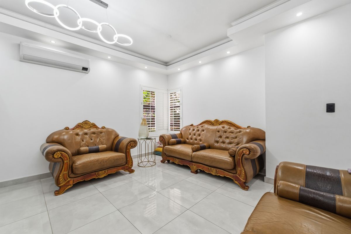 Bright living room featuring polished porcelain floor tiles, recessed ceiling lighting, crown molding, and a wall-mounted air conditioning unit.